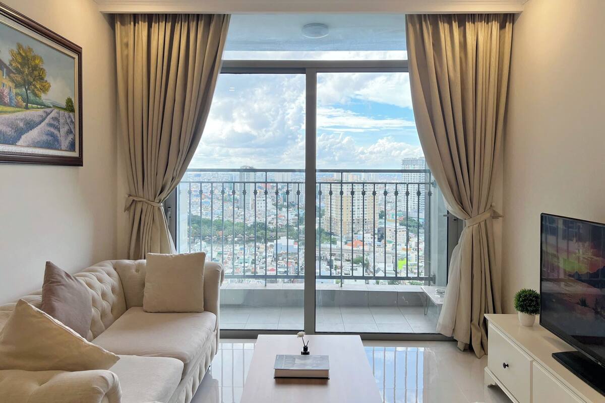 A modern living room with a sofa, a coffee table, a TV, and a balcony with a city view.