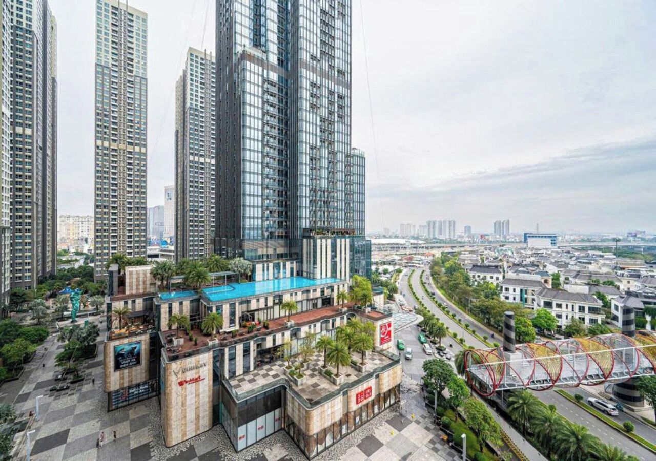 A high-rise building with multiple floors, surrounded by other tall buildings, and a busy road with a pedestrian bridge.