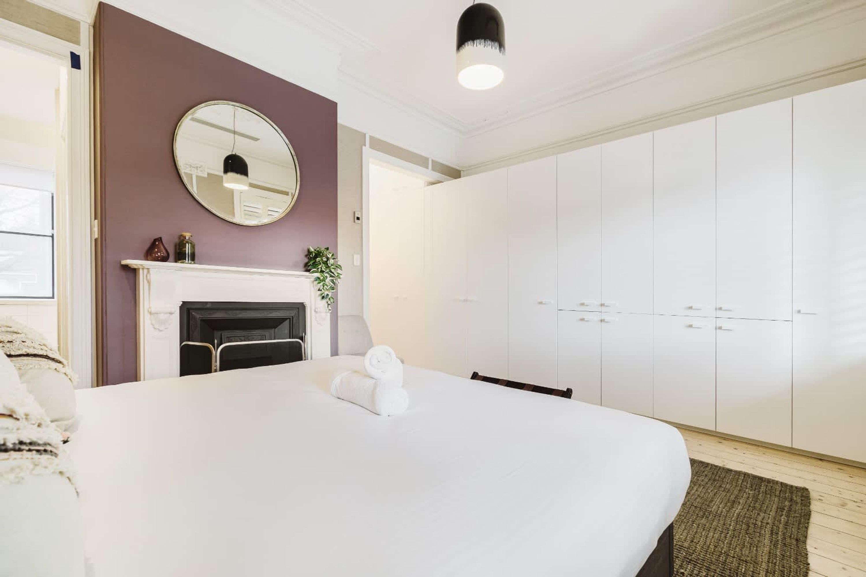 Un dormitorio con una cama grande, chimenea, armario y espejo en la pared.