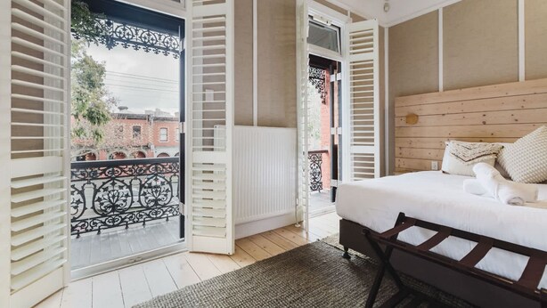 Una camera da letto con un letto, una testiera in legno, un termosifone e un balcone con persiane aperte.