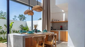 A modern kitchen with a large island, wooden chairs, and hanging wicker lights. - Dela Villa by Betterplace (Pecatu)