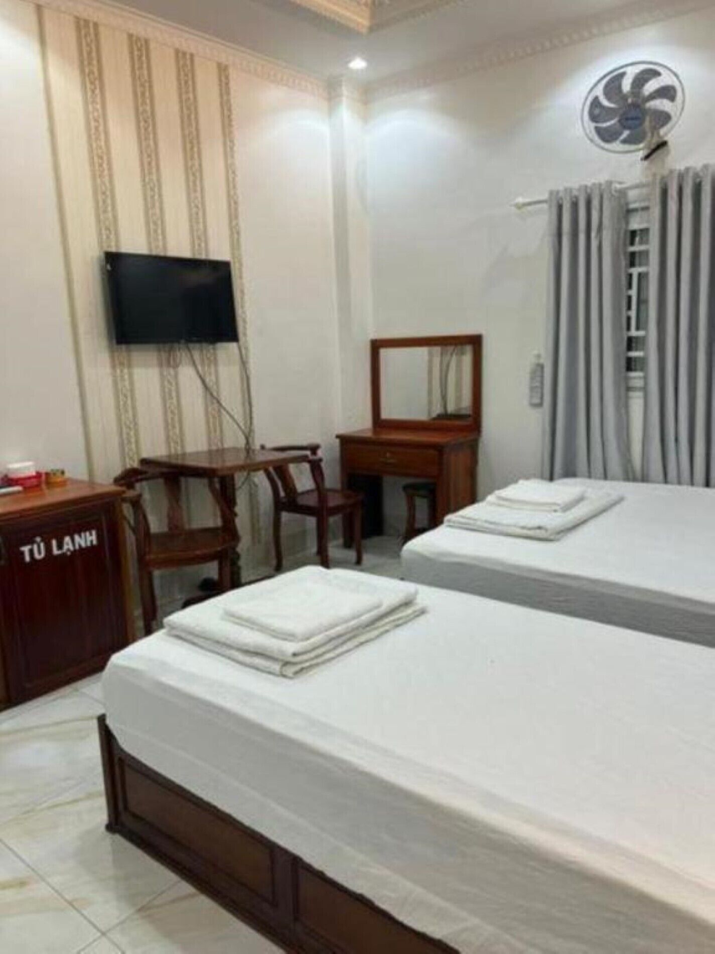 A hotel room with two beds, a desk, a chair, a television, and a fan.