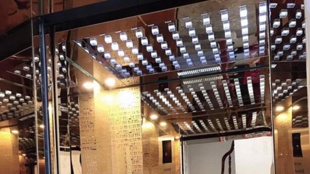 L’intérieur d’un ascenseur avec des parois métalliques, une porte en verre et un plafond doté de luminaires.