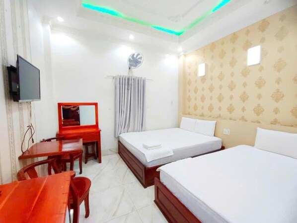 Una habitación de hotel con una cama, un escritorio con espejo, un televisor y un ventilador de techo.