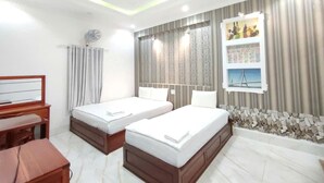 Une chambre d’hôtel avec deux lits, un bureau, une chaise, une fenêtre avec des rideaux et un mur agrémenté d’une étagère décorative.