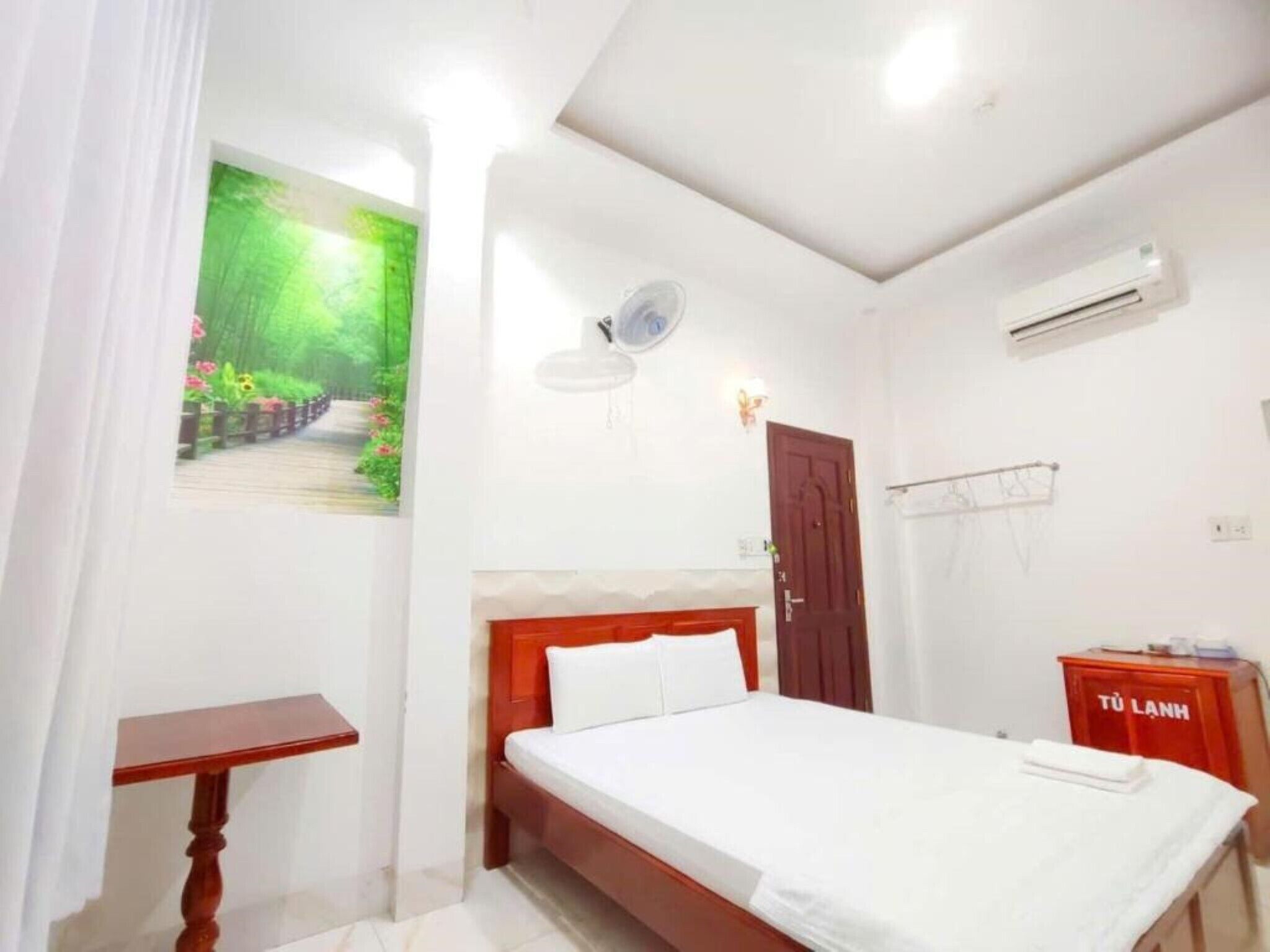 A bedroom with a bed, a small table, a wall-mounted air conditioner, and a door.