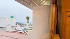 A rooftop terrace with a wooden door, a white railing, and a view of the surrounding landscape. - Wanderlust Mukteshwar (Dhari)