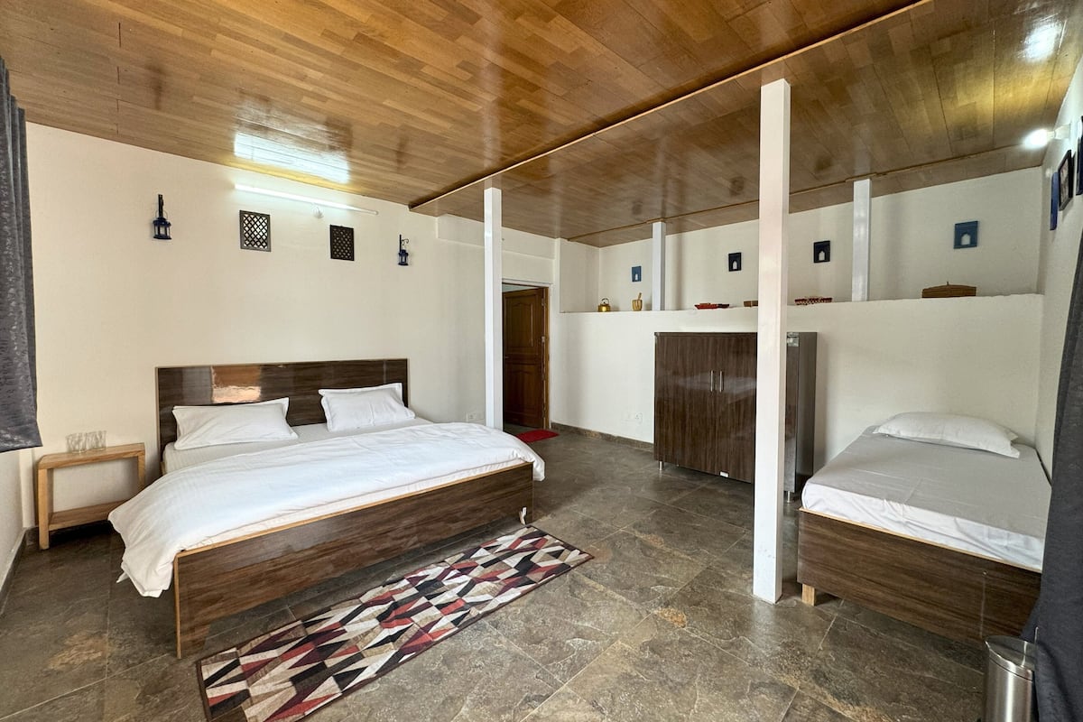Une chambre avec un grand lit, un plus petit lit et une armoire.
