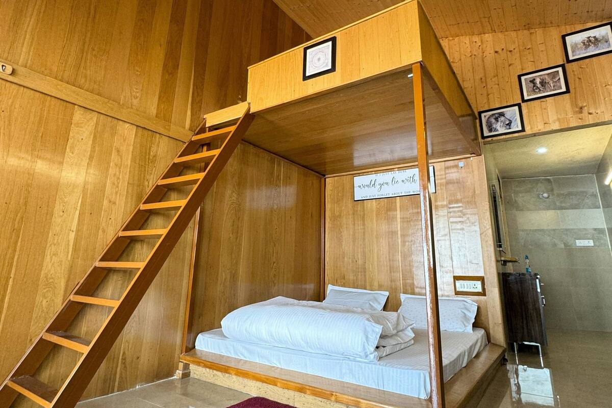 Une chambre avec un lit superposé en bois, une échelle, un petit tapis et des tableaux encadrés accrochés au mur.