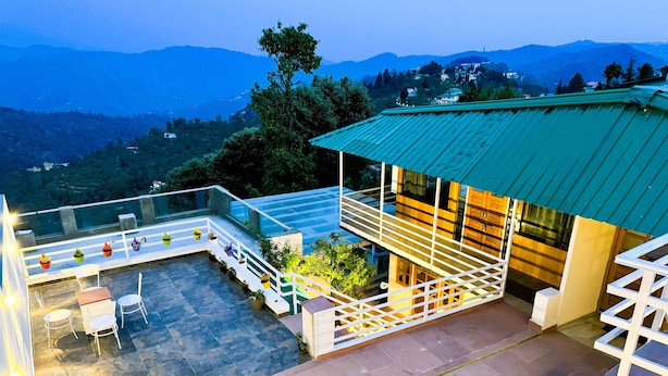 A rooftop terrace with outdoor seating, a staircase, and a view of the surrounding hills. - Wanderlust Mukteshwar (Dhari)