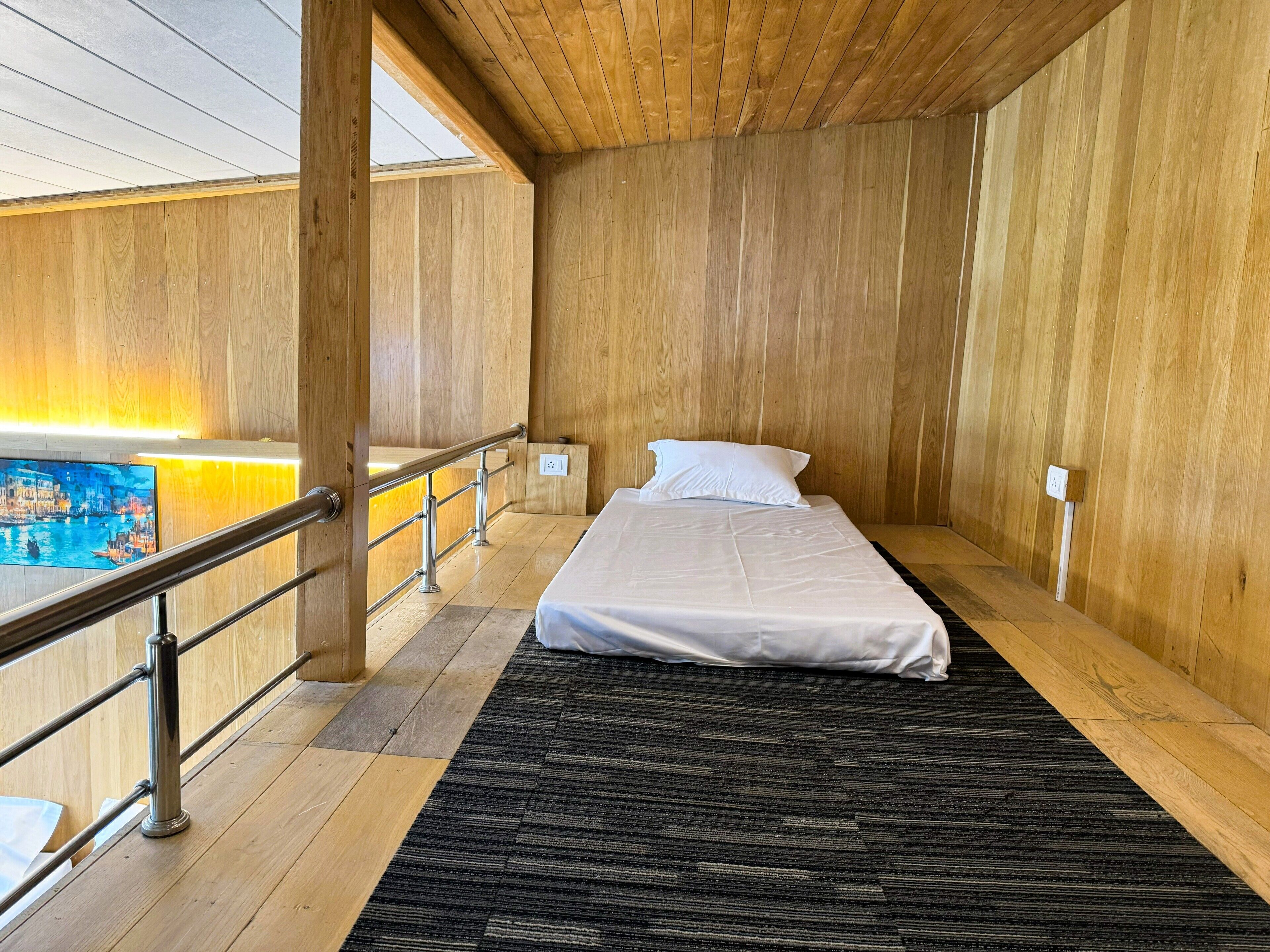 A wooden room with a bed, a view of a cityscape, and a railing.