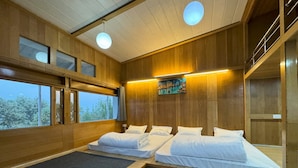 A modern hotel room with wooden walls, two beds, a large window, and a painting on the wall. - Wanderlust Mukteshwar (Dhari)