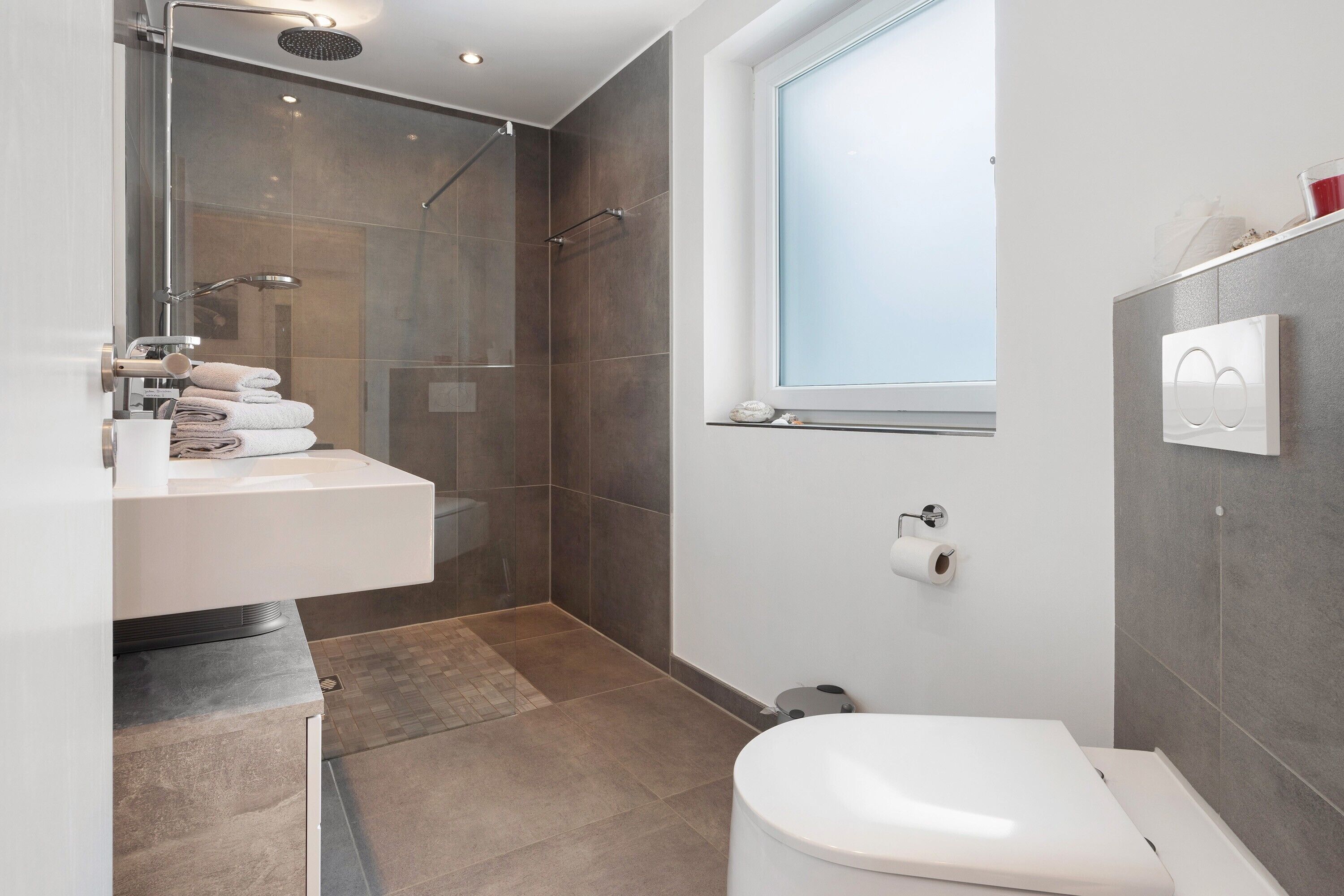 A modern bathroom with a glass shower enclosure, a toilet, and a sink with a towel rack.