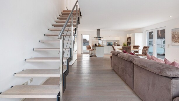 A modern interior with a staircase, a kitchen area, and a seating area with a sofa.