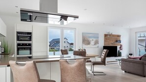 A modern kitchen with built-in ovens, a dining area with bar stools, a sofa, and a fireplace.