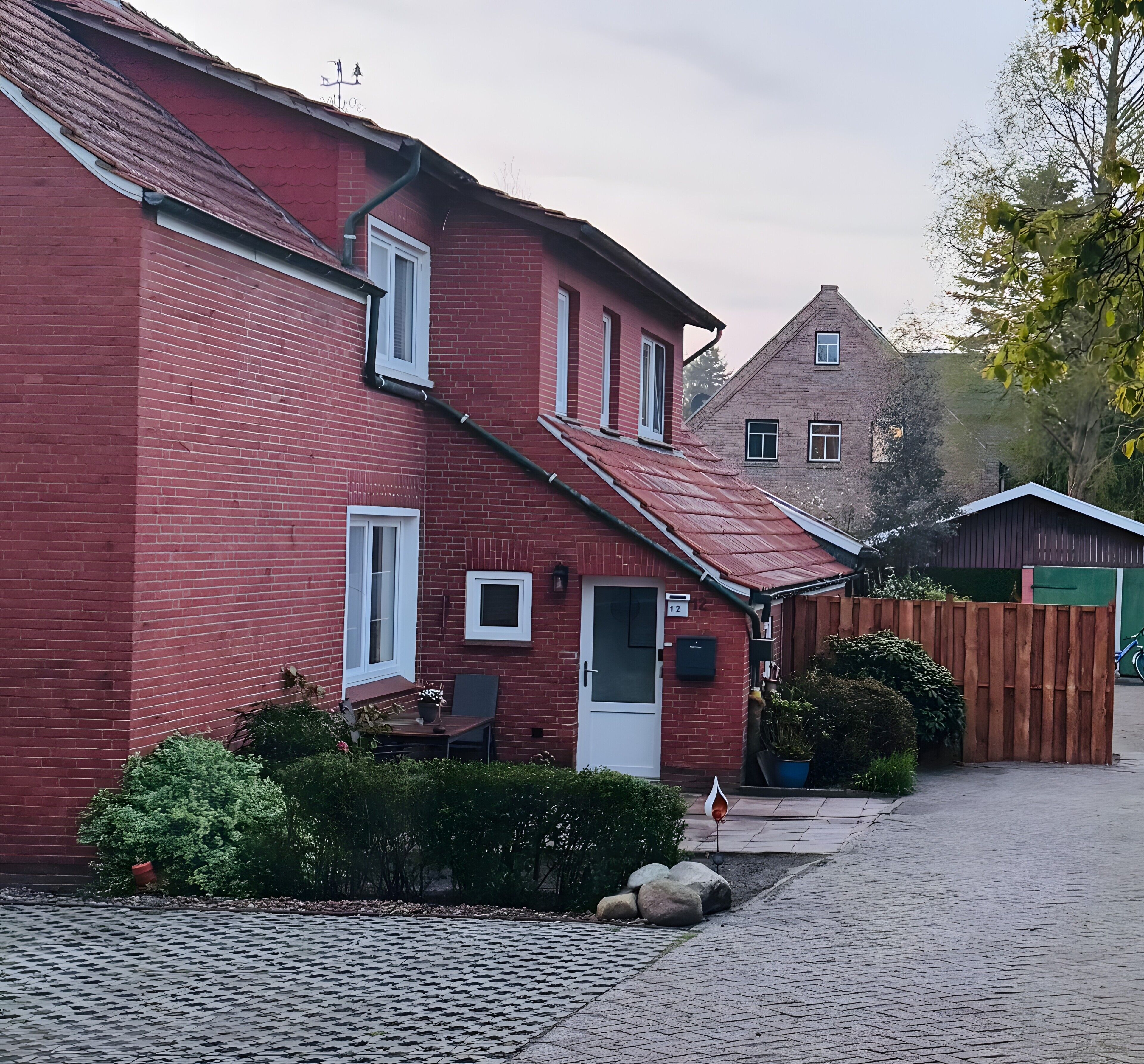 Ein rotes Backhaus mit geneigtem Dach, einer Haustür und einer kleinen Veranda mit Tisch und Stuhl.