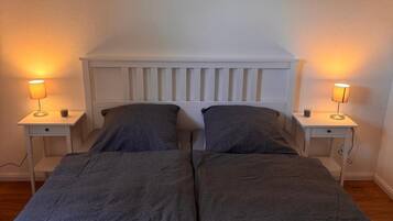 A double bed with a white headboard, two bedside tables with lamps, and a plain wall.