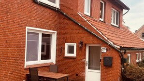 A red brick house with a tiled roof, a front door, and a small table with chairs outside. - Apartment 'Ferienwohnung Liese' with Private Terrace, Private Garden and Wi-Fi (Detern)