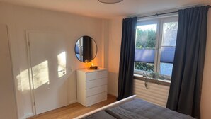 A bedroom with a bed, a dresser, a mirror, and a window with curtains. - Apartment 'Ferienwohnung Liese' with Private Terrace, Private Garden and Wi-Fi (Detern)