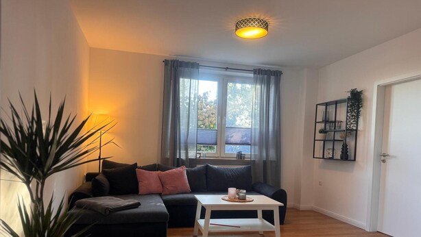 A living room with a sofa, a coffee table, a potted plant, a window with curtains, and a wall-mounted shelf. - Apartment 'Ferienwohnung Liese' with Private Terrace, Private Garden and Wi-Fi (Detern)