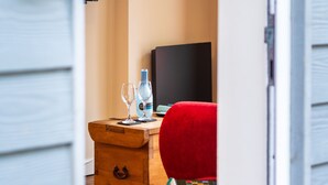 A wooden chest of drawers with a bottle and glasses on top, a red chair, and a blackboard in the background. - Jetty Cottage by Interhome (Mevagissey)