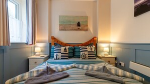 A bedroom with a bed featuring striped bedding, a wooden headboard, and two bedside tables with lamps. A painting of a beach scene is on the wall above the bed. - Jetty Cottage by Interhome (Mevagissey)