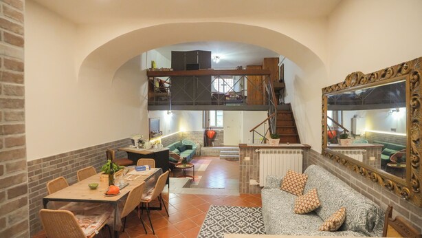 Une salle à manger spacieuse avec un plafond haut, un escalier menant à un niveau supérieur et un grand miroir sur le mur.