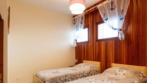 Una habitación con dos camas de madera, una pared de madera, una lámpara en el techo y una ventana con cortinas.