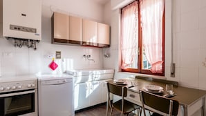 Cocina compacta con estufa, horno, lavavajillas y un pequeño comedor con mesa y sillas.
