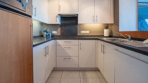 A modern kitchen with white cabinetry, a black countertop, and a stainless steel microwave. - Marebelle with seaview by Interhome (Bredene)
