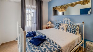 Une chambre à coucher avec un lit, une table de chevet, un miroir et une fenêtre avec des rideaux.