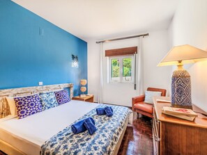 Une chambre à coucher avec un lit, une table de chevet, une lampe, une chaise et une fenêtre.