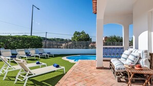 Un área junto a la piscina con sillones, una mesita y un espacio de estar cubierto.