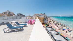Une terrasse sur le toit, avec des chaises longues, une table et une vue sur la plage et le paysage urbain.