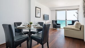 Un coin repas avec une table en verre, des chaises noires et une vue sur la mer, visible à travers une grande fenêtre.