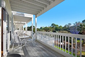 A covered porch with white railings, outdoor seating, and a view of the surrounding greenery and buildings. - Renovated 2-Bed Townhome on 30A w/ Pools, Hot Tub, & Steps to Spooky Lane Beach Access! (Santa Rosa Beach)