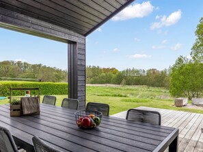 An outdoor patio with a table and chairs, a fruit bowl, and a view of a grassy field and trees.