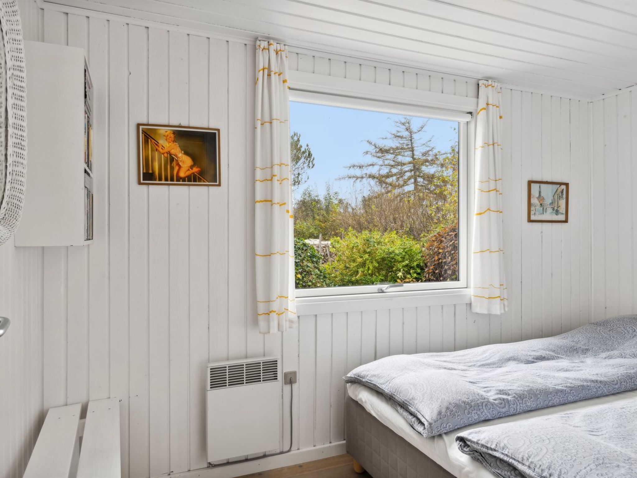 A bedroom with a bed, a window with curtains, a radiator, and a wall-mounted heater.