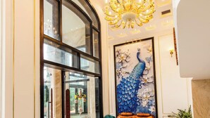 Un lobby espacioso con una imponente lámpara de araña, un mural de pavo real y un área de descanso con sillones tapizados en tonos turquesa y marrón.