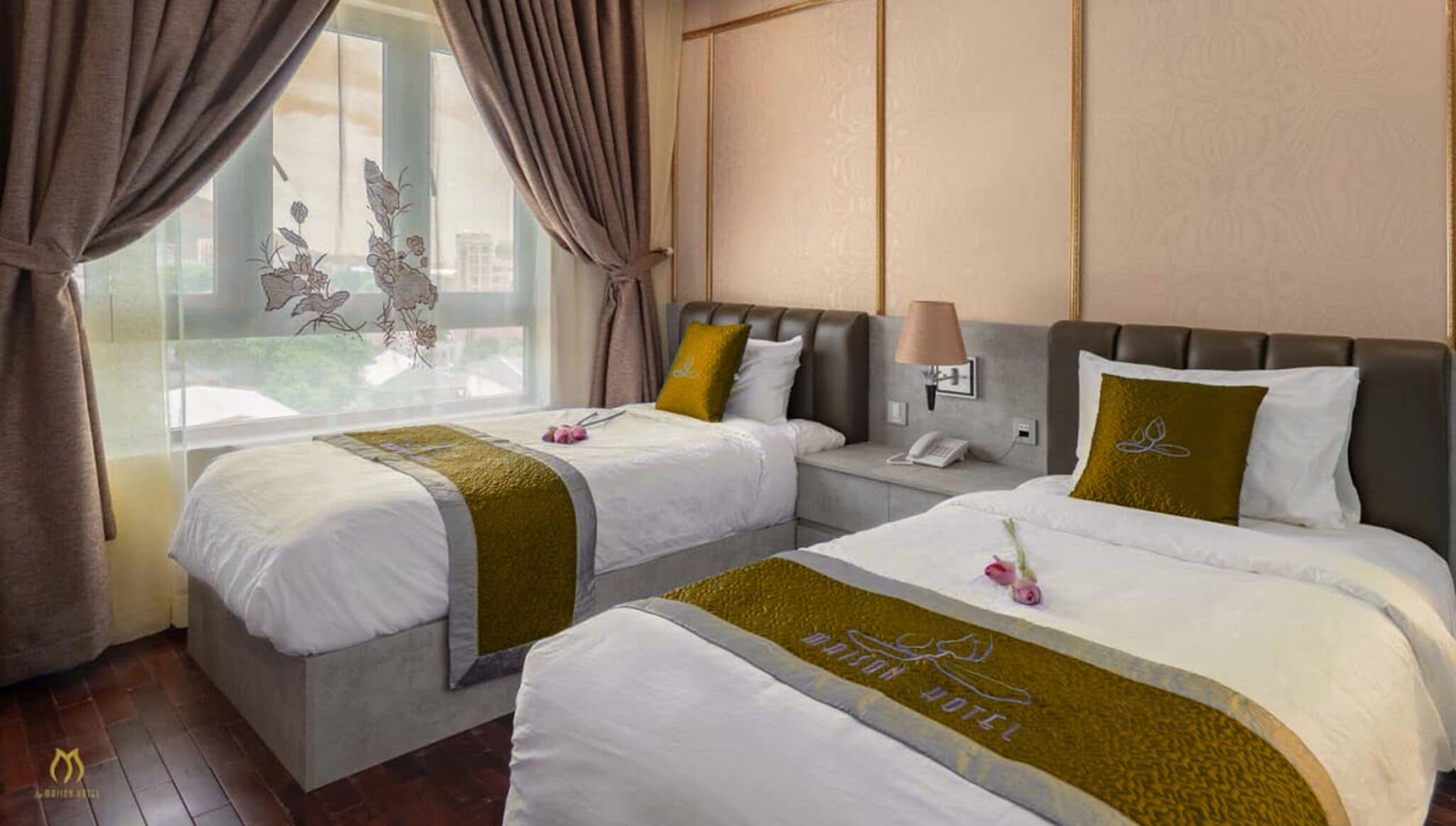 A hotel room with two beds, a nightstand, a lamp, and a window with curtains.