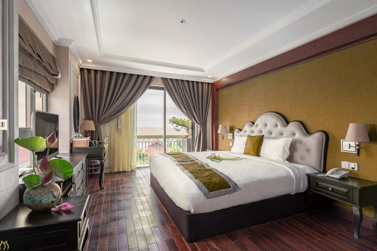 Amplia habitación de hotel con una cama grande, un escritorio con silla, una lámpara de escritorio, un teléfono y vistas al exterior.