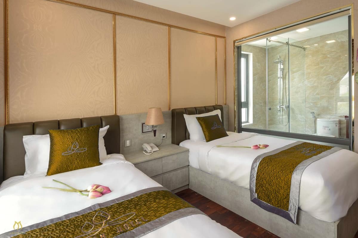 Habitación de hotel con dos camas, una mesita de noche, una lámpara, un espejo y zona de ducha.