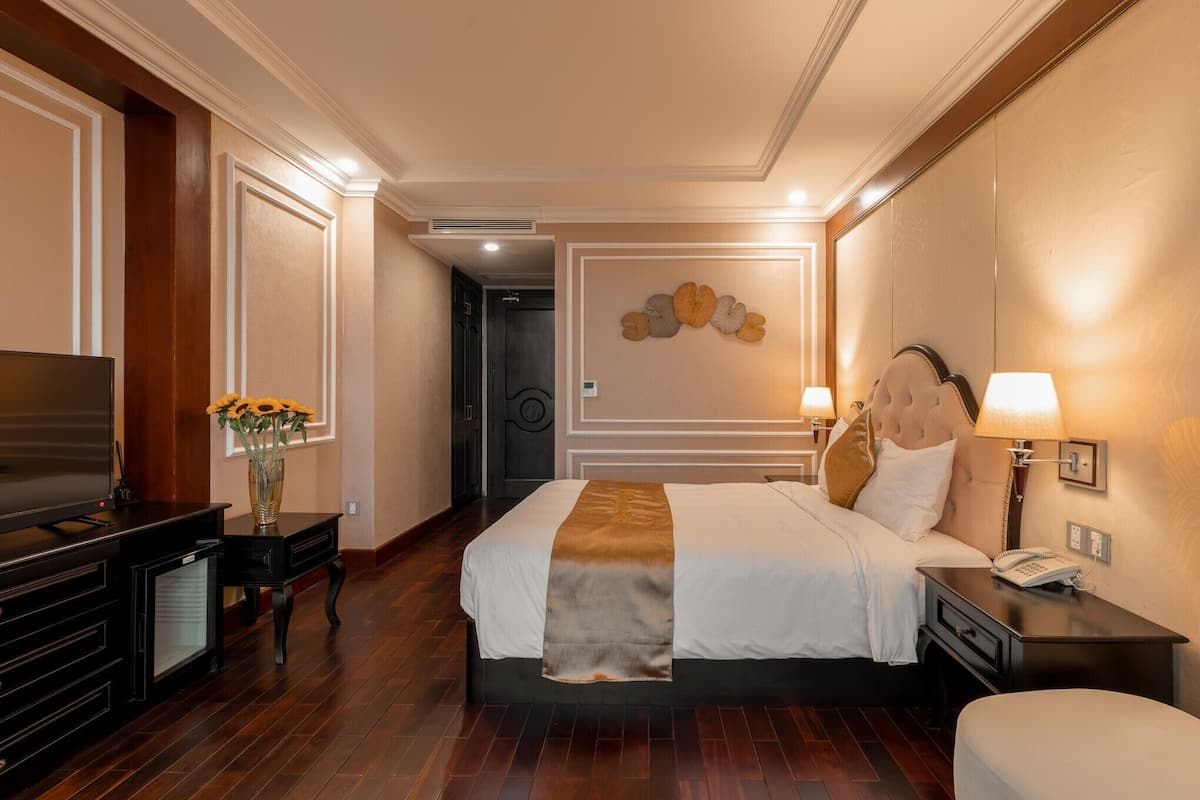 Habitación de hotel con una cama grande, un televisor, un escritorio con lámpara y una obra de arte colgada en la pared.
