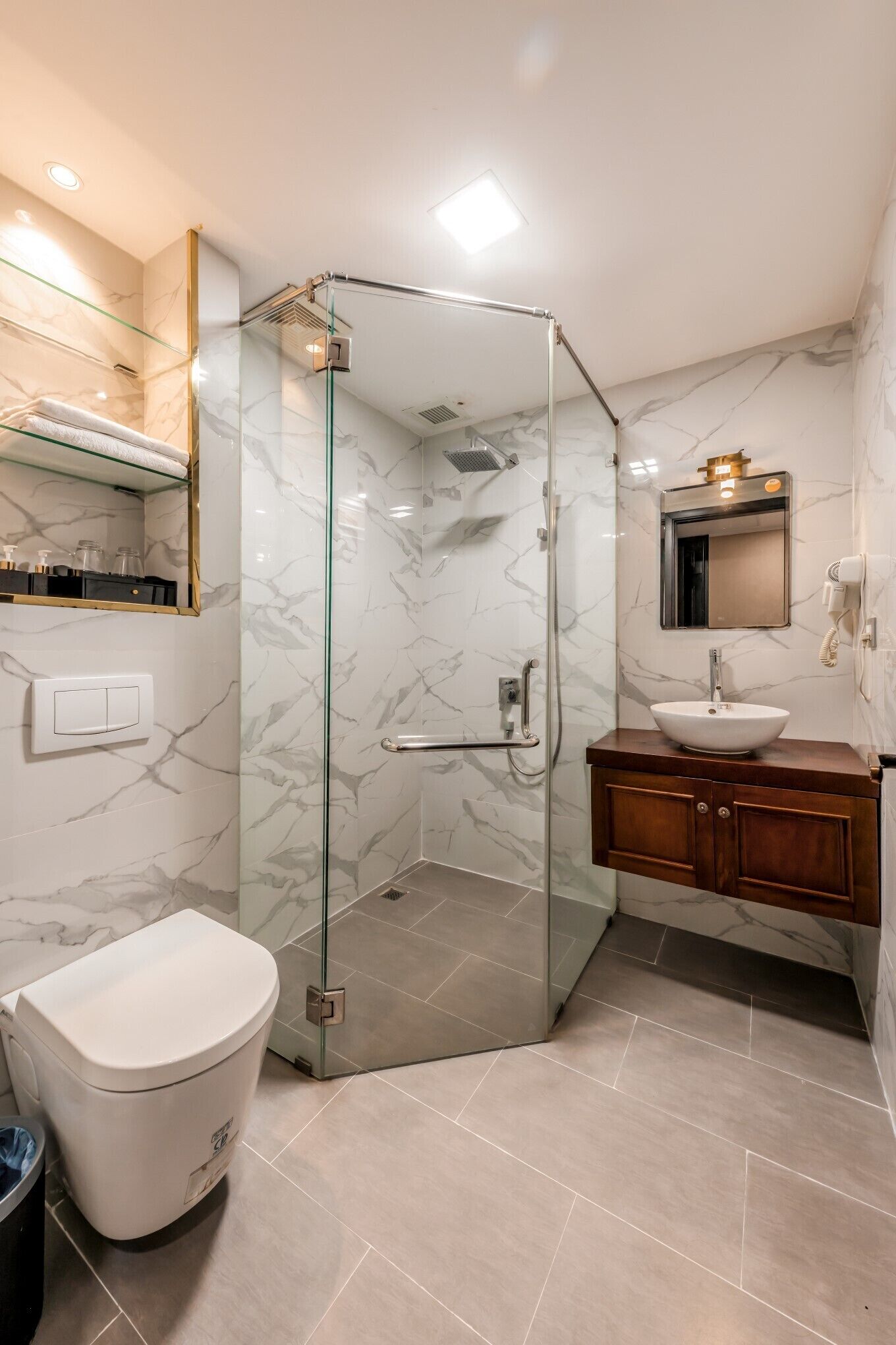 Un baño moderno con ducha de vidrio, inodoro blanco y tocador de madera con lavamanos.