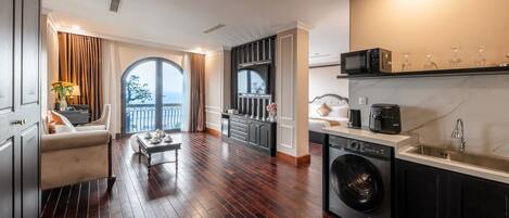 A modern hotel room with a large balcony, a kitchen with a washing machine, and a dining area with a sofa and table.