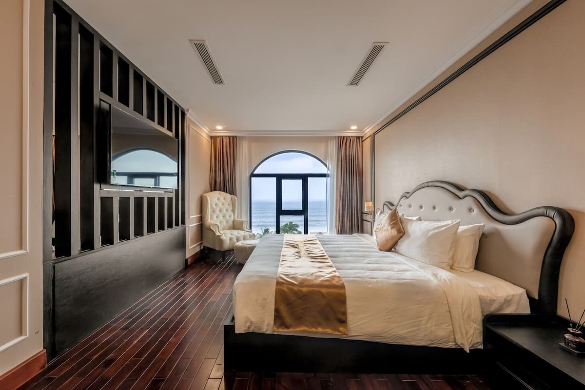 Un dormitorio con una cama grande, una silla, un televisor y vista al mar.
