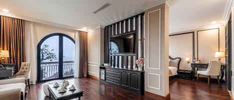 A spacious living room with a large TV, a comfortable seating area, and a balcony with a view.