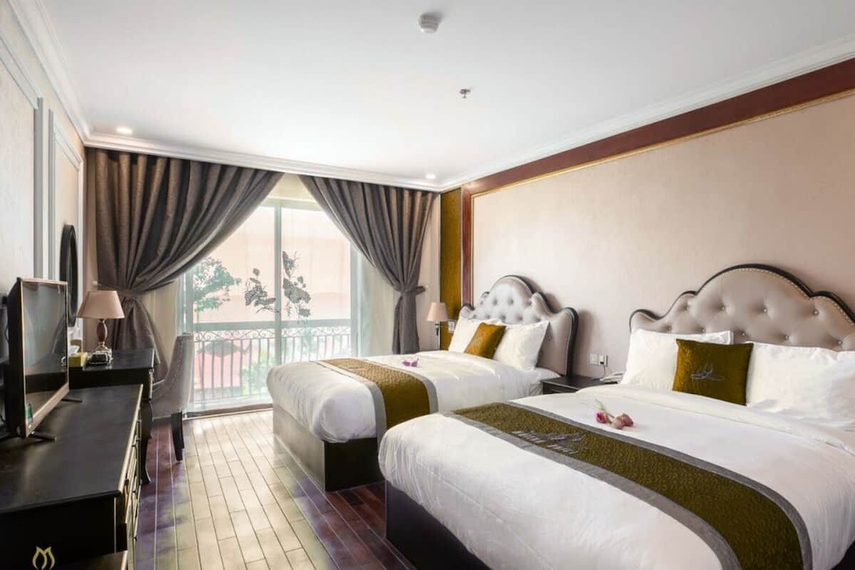 Habitación de hotel con dos camas, un escritorio y un balcón con cortinas.