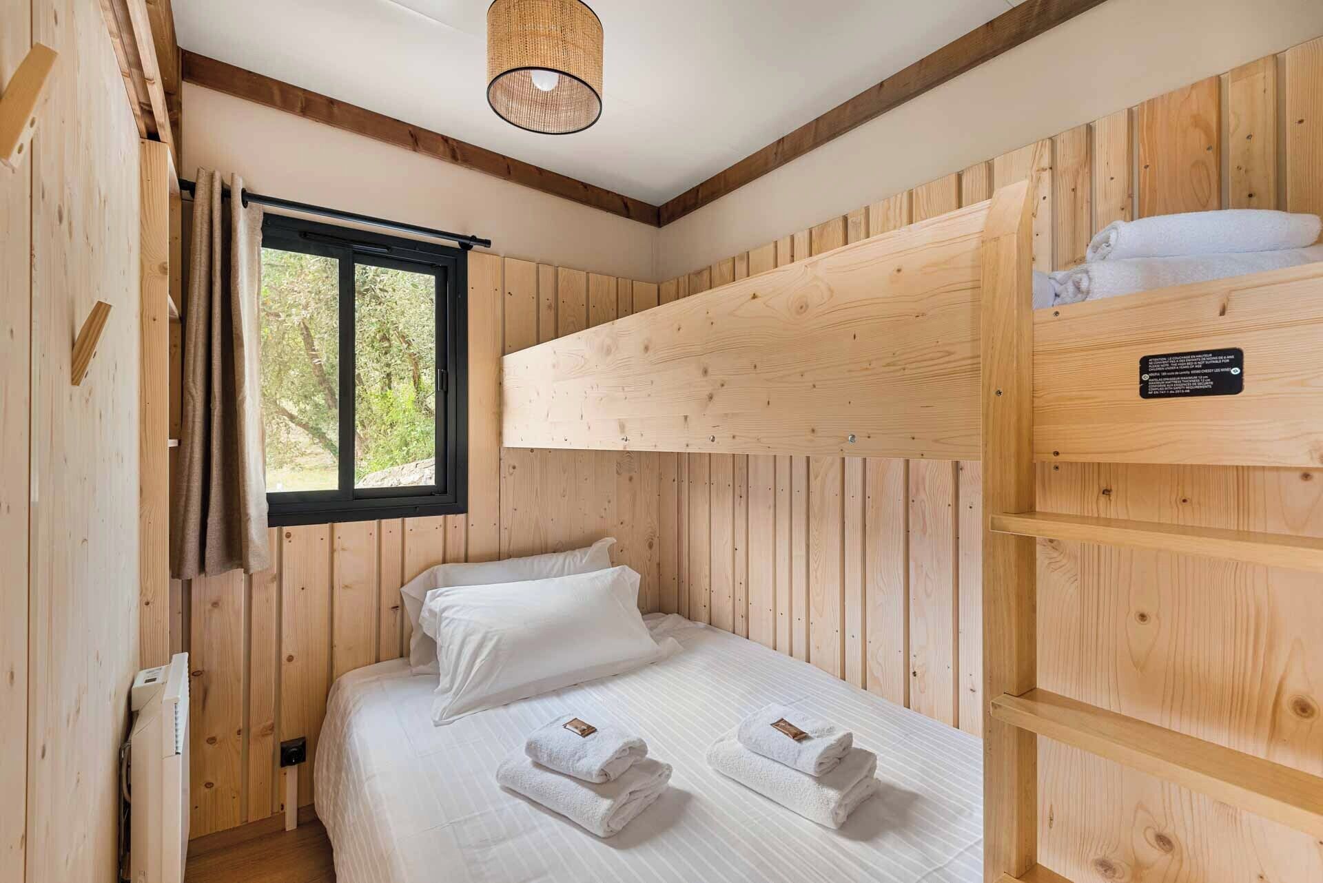 Een houten kamer met een stapelbed, een raam met gordijnen en een hanglamp.
