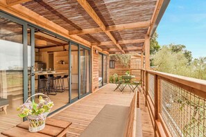Eine Holzdar Terrasse mit Tisch und Stühlen, ein Korbwägelchen mit Blumen und Blick auf die umliegende Landschaft.